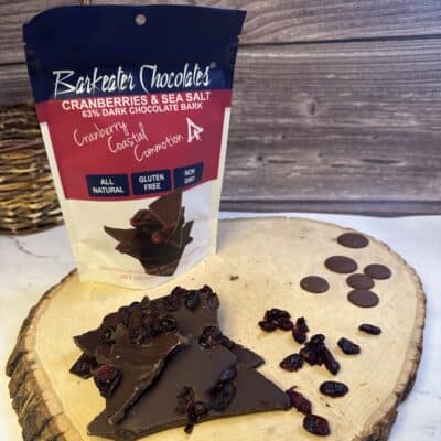 Loose dark chocolate with cranberries on wood slab. Pouch behind it.