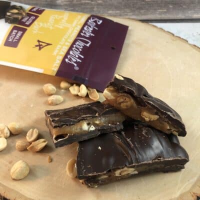 Caramel dark chocolate bark with peanuts loose on wood slab with pouch in background