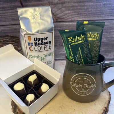 Open box of truffles, bag of coffee, chocolate bars and a mug on a wood slab