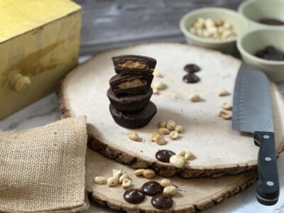 cut up peanut butter cups with peanuts and a knife on wood slab